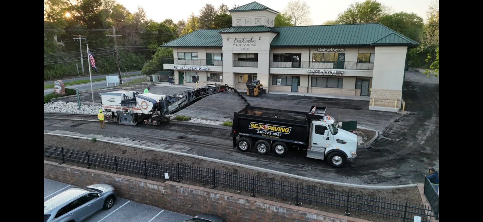 Cold planer milling asphalt on a commercial parking lot with a SEJ Paving dump truck hauling milled material