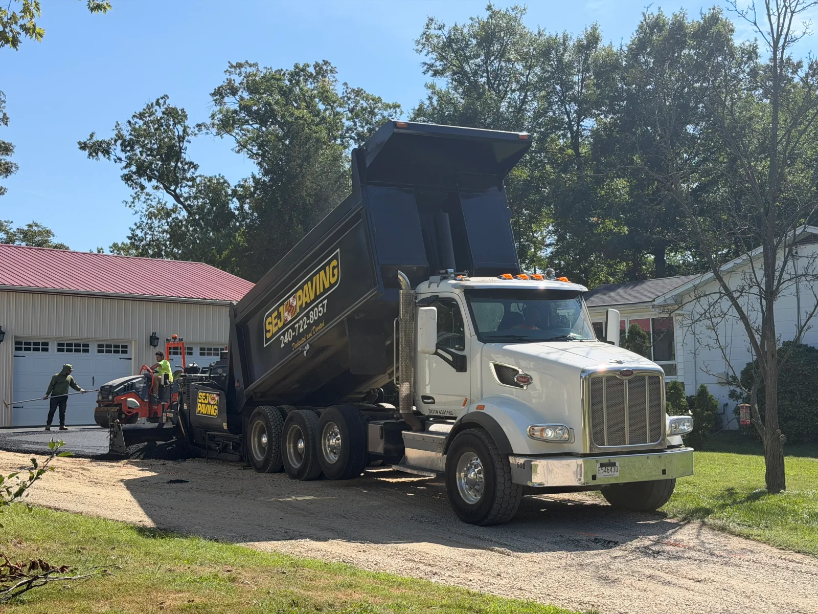 Dump truck unloading hot asphalt into a paver laying a new driveway with crew raking the mix